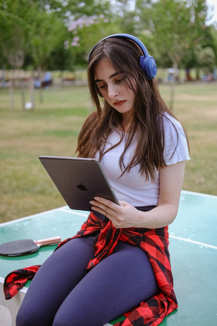 A girl with headphones and a tablet sitting on a bench